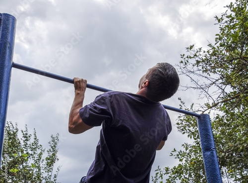 The man pulls himself up on the bar. Playing sports in the fresh air. Horizontal bar.