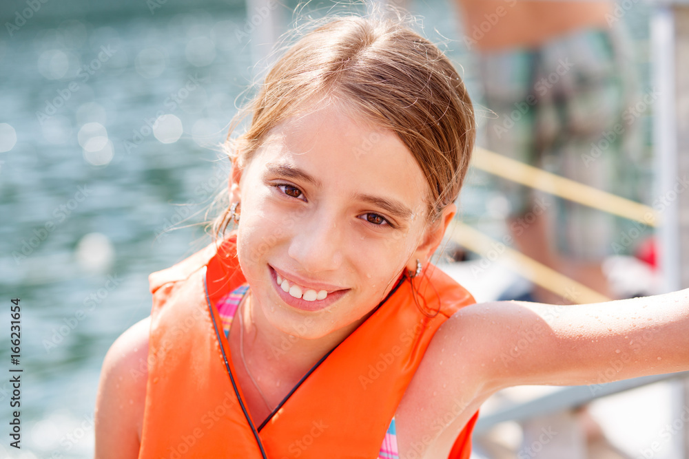 Happy teenage girl in orange life vest at beach