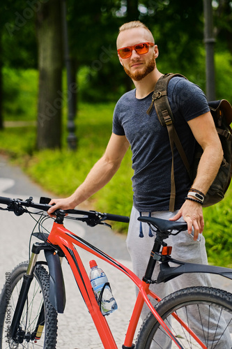 A man sits on a red mountain bicycle outdoor.
