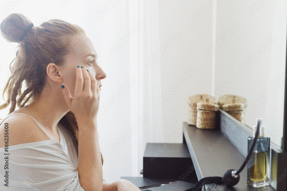 Ginger woman with dreadlocks is making up herself in front of the mirror in bedroom Ginger woman with dreadlocks is making up herself in front of the mirror in bedroom