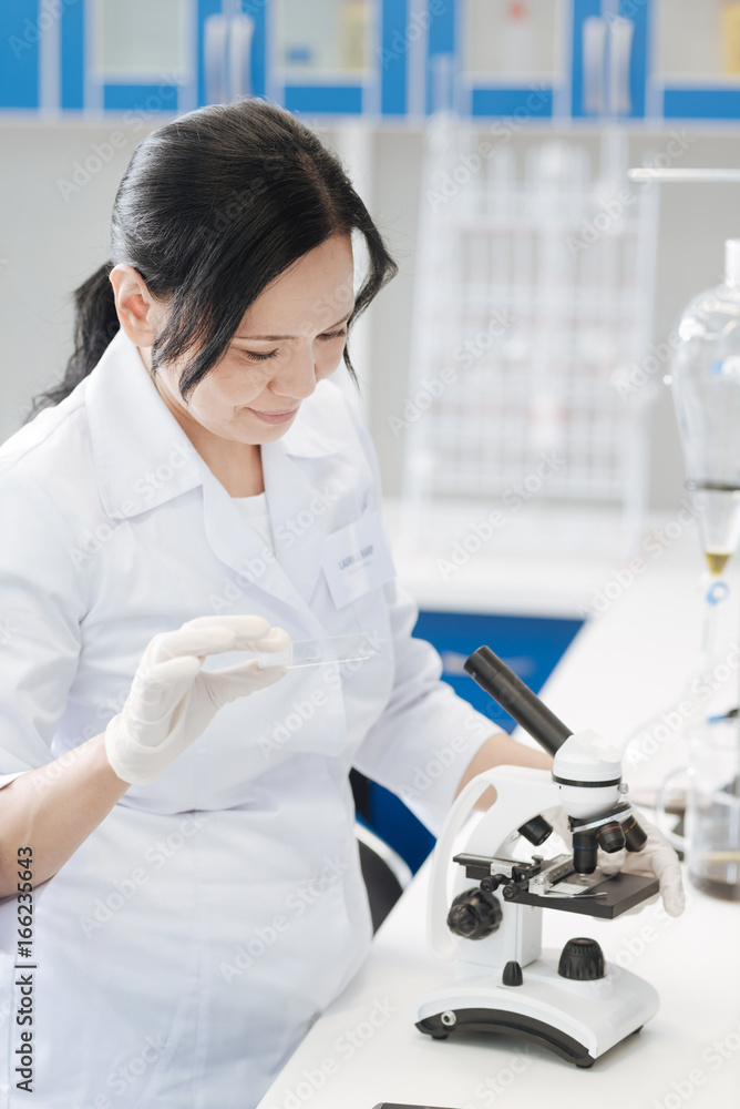 Pleasant professional biologist holding a microscope slide Pleasant professional biologist holding a microscope slide