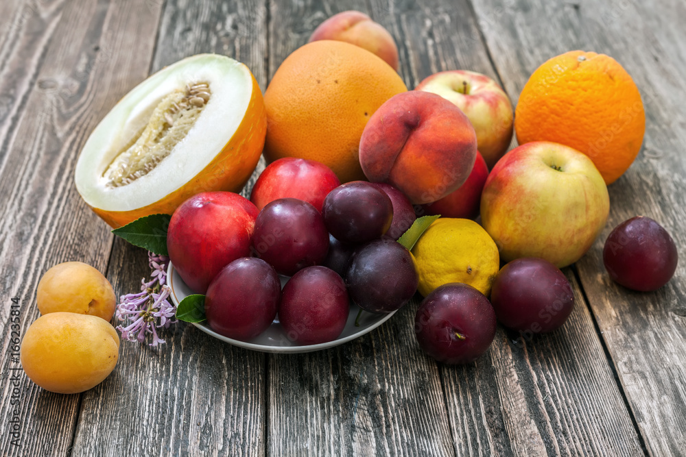 Melon, apples, plums, lemon, peaches, apricots and grapefruit on a wooden table.