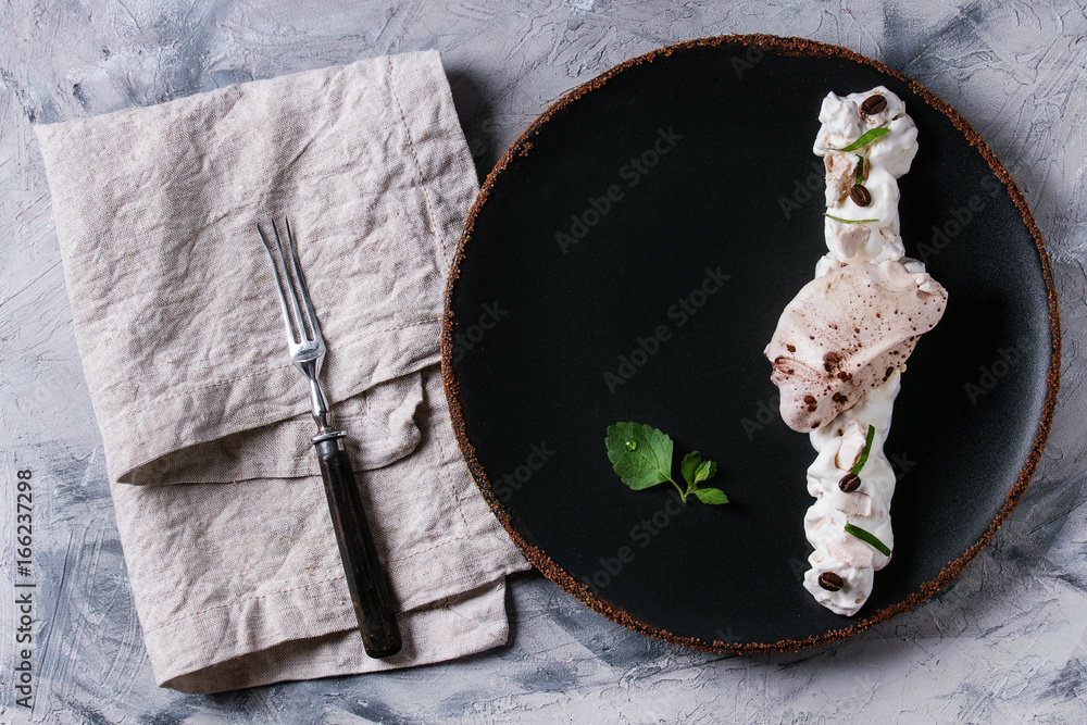 Food plating french dessert chocolate meringue with fresh mint, whipped  cream and coffee beans served with fork and textile napkin on black plate  over gray concrete texture background. Flat lay, space Photos