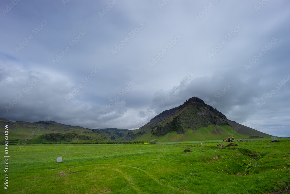 Iceland - Green meadow with dredger and mountain Iceland - Green meadow with dredger and mountain
