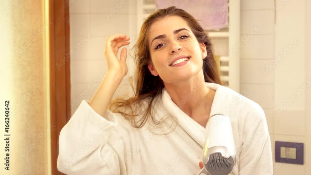 Beautiful happy woman blow drying long hair looking camera smiling super slow motion closeup warm light Beautiful happy woman blow drying long hair looking camera smiling super slow motion closeup warm light
