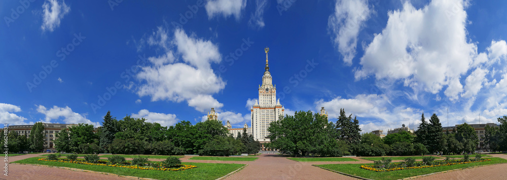Wide angle frontal panoramic landscape view of light clouds over the sunny summer campus of Lomonosov Moscow State University under blue sky