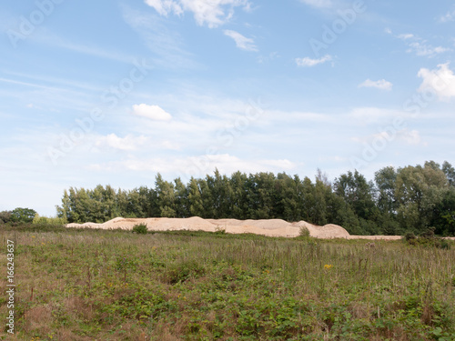 piles of sand from quarry in distance of field with sky above