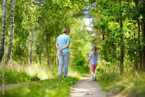 Cute little girl hiking in a forest with her grandmother on beautiful summer day