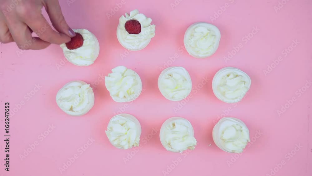 Petit Fours presentation of meringues with raspberries and rose petals on pink wood overhead time lapse. Petit Fours presentation of meringues with raspberries and rose petals on pink wood overhead time lapse.