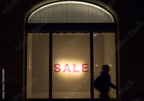 Bilde på lerret Silhouette of  woman walking in blurry motion in front of a fashion store's window in night