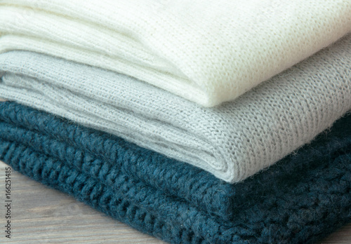 A few stacked warm knitted sweaters, lying on a wooden background. The concept of warm.