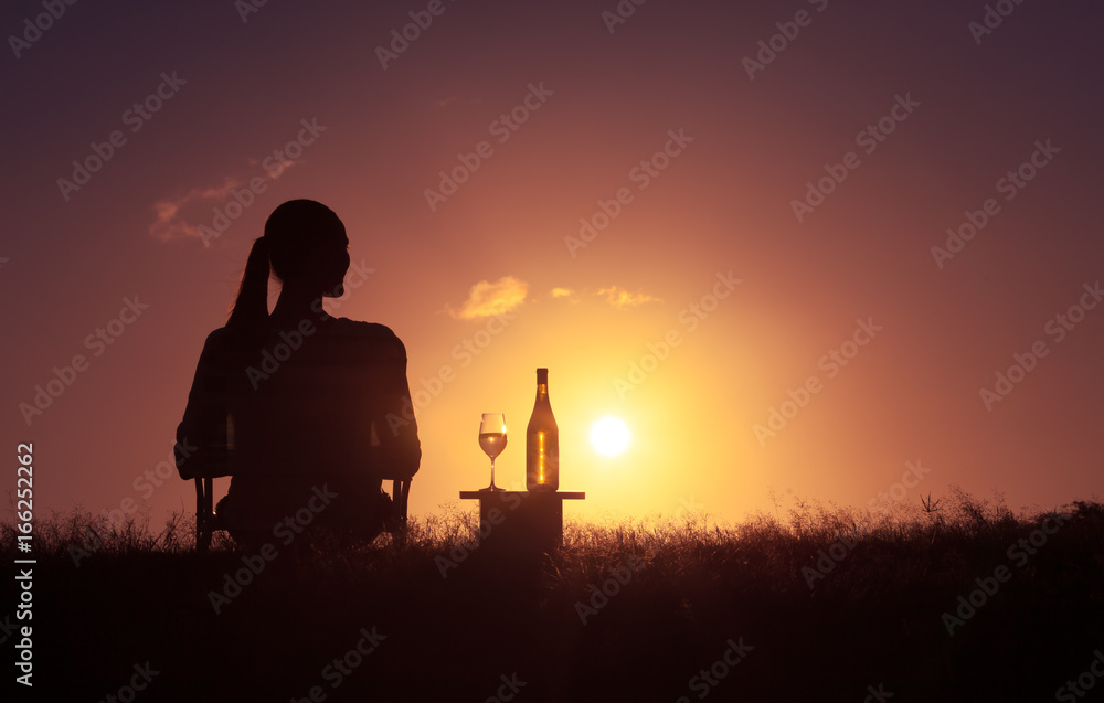 People relaxing nature. Woman sitting in a chair in a open field enjoying a glass of wine and a beautiful sunset. 