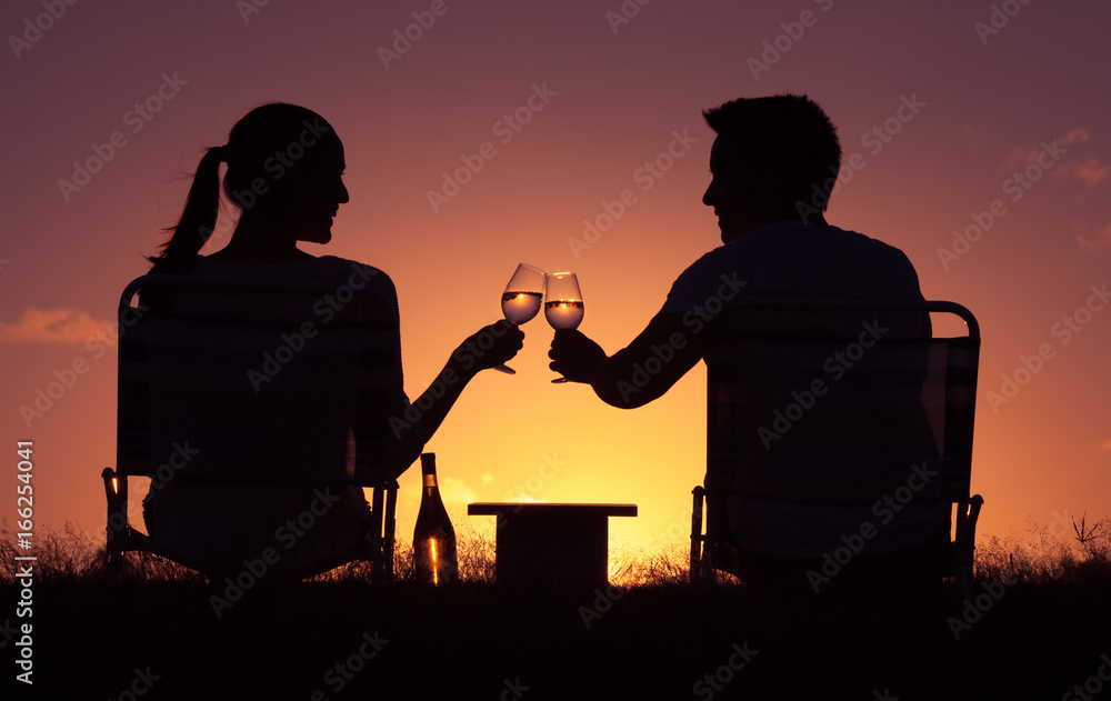 People in love, happy lifestyle moments. Man and woman toasting wine glasses against a sunset background.
