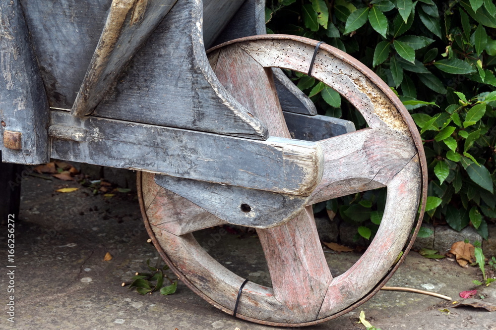 Rustic wooden wheelbarrow wheel, on stone track with leaves in background