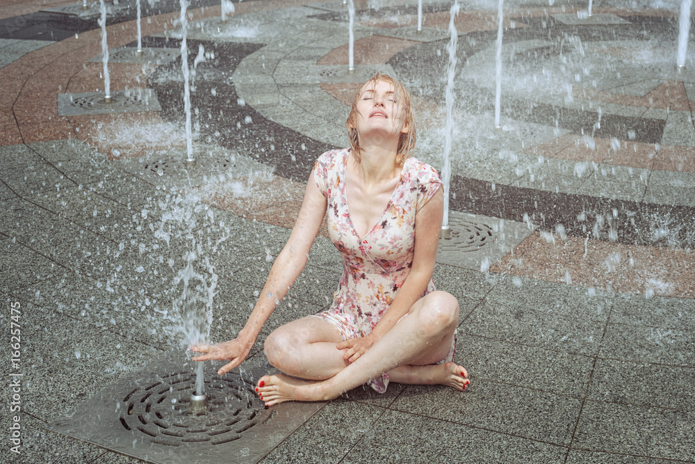 Woman sits in a fountain, she is all wet. Stock Photo Adobe Stock