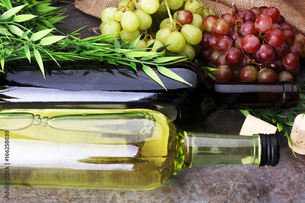 Obraz premium Bottle of white and red wine, grape and corks on wooden table