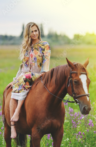 Young woman sits on a horse in a summer meadow