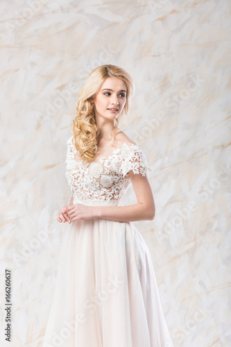 fashionable wedding dress, beautiful blonde model, bride hairstyle and makeup concept - romantic young woman in luxury white gown indoors on light background, perfect female posing in the studio