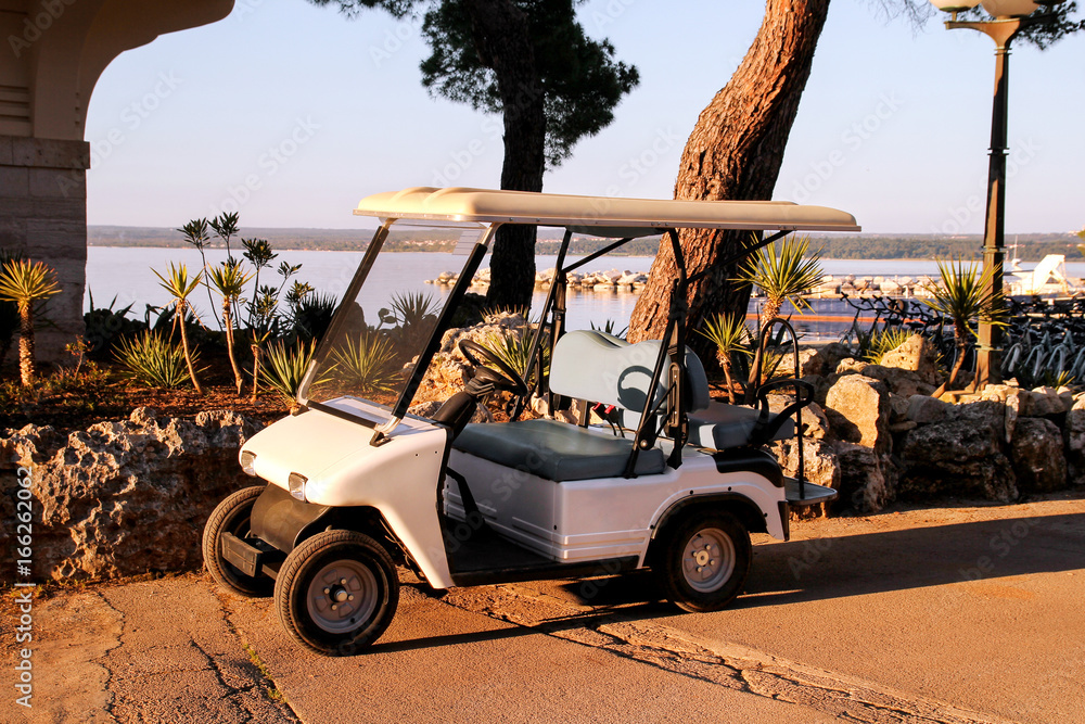 Golf car parked in outdoors on a sunny spring day. White golf club car.