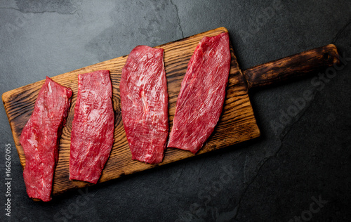 Fresh raw meat beef steaks. Beef tenderloin on wooden board, spices, herbs, oil on slate gray background. Food cooking background concept