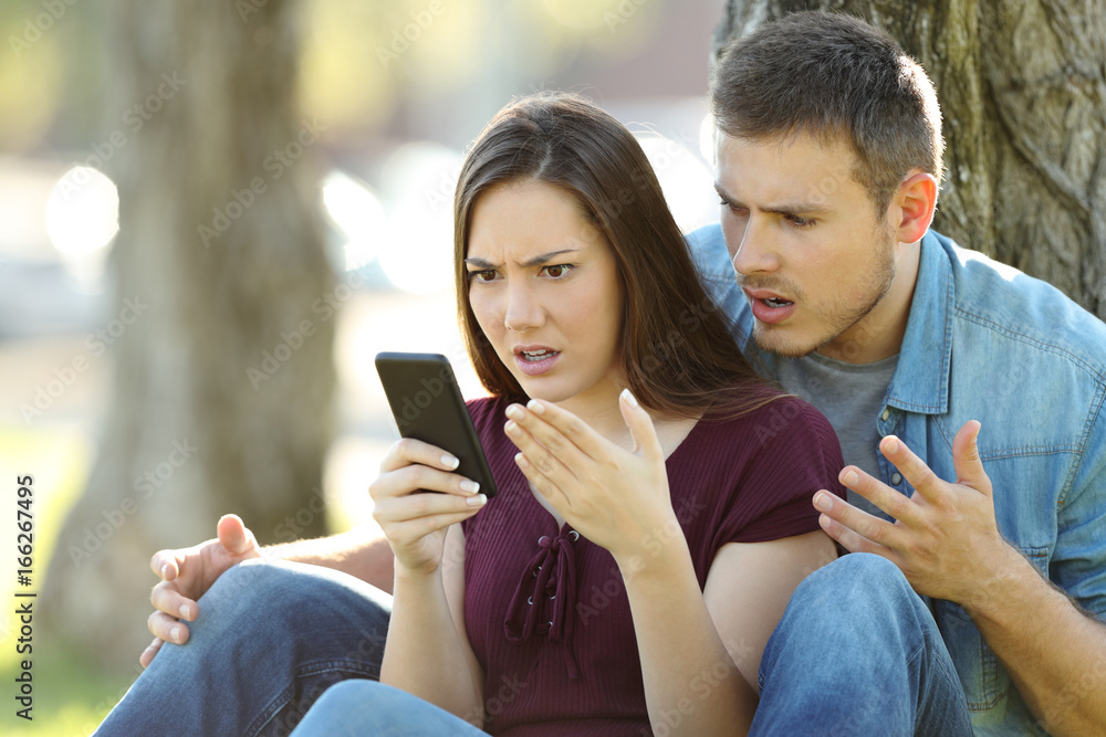 Angry couple using a smart phone outdoors Angry couple using a smart phone outdoors