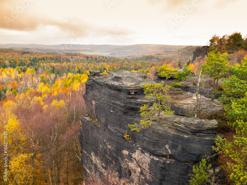 Sandstone rock formation in the middle of colorful autumn forest. Dramatic evening view. Tisa Rocks, aka Tiske Walls, Czech-Saxon Switzerland, Czech Republic