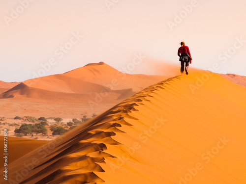 Woman walking on the ridge of red dune in windy weather, Sossusvlei, Namib desert, Namibia.