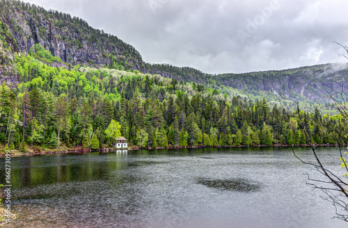 Lake house in summer landscape by water during rainy cloudy day in Quebec, Canada