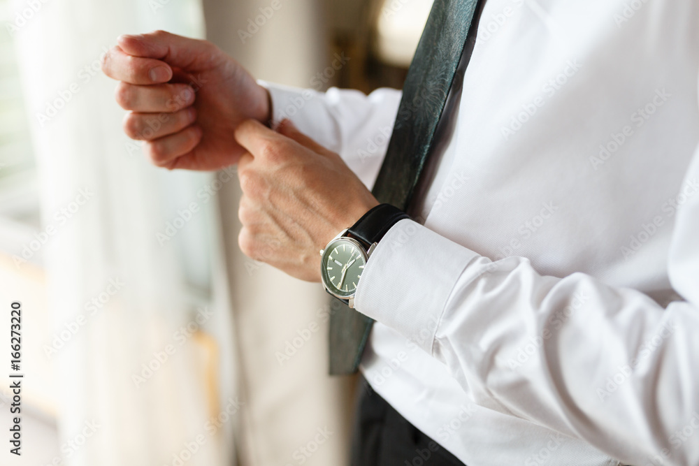 Naklejka premium Businessman adjusting his cuffs on the sleeves white shirt. Portrait of a man who straightens his cufflinks. On a hand expensive watch. Against the background of an expensive hotel. close-up.