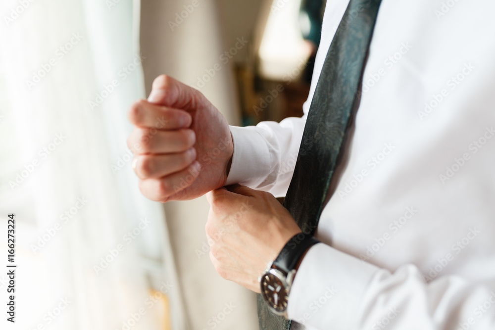 Businessman adjusting his cuffs on the sleeves white shirt. Portrait of a man who straightens his cufflinks. On a hand expensive watch. Against the background of an expensive hotel. close-up.