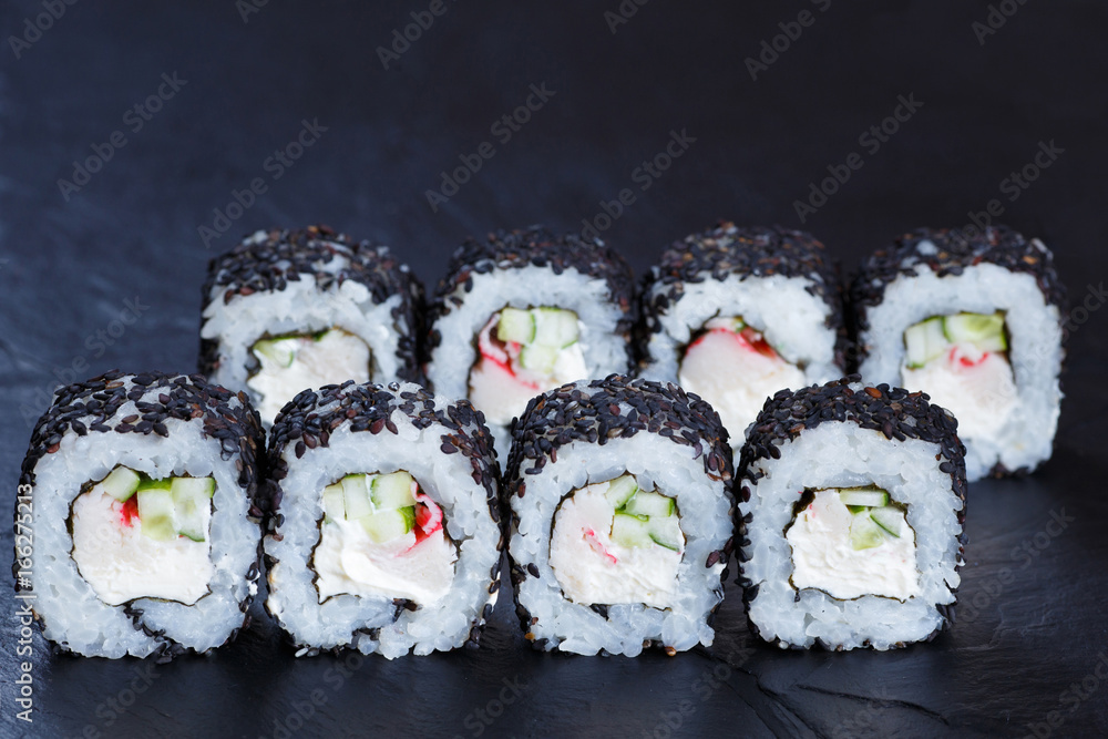 Tasty Japanese food. Sushi rolls with crab meat, cucumber and cream cheese, covered with black sesame, served on black stone slate Tasty Japanese food. Sushi rolls with crab meat, cucumber and cream cheese, covered with black sesame, served on black stone slate