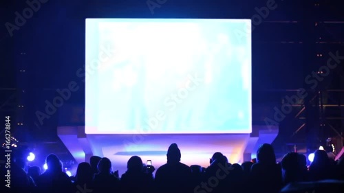 A crowd of people at the concert watches the performance. Artists on stage dance and sing songs. Above Scoreboard for capturing and displaying video. White background instead of green.