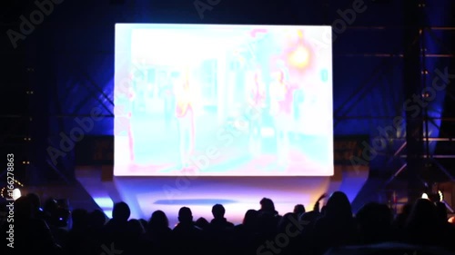 A crowd of people at the concert watches the performance. Artists on stage dance and sing songs. Above Scoreboard for capturing and displaying video. White background instead of green.