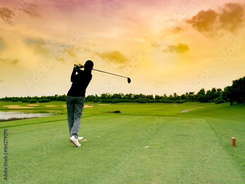 Lady golfer, girl golf player hit the golf ball with full swing, follow through on the tee at sunrise beautiful golf course