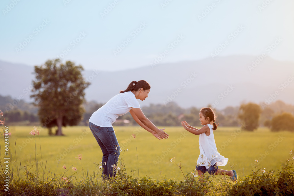 Cute asian child girl running to her mother to give a hug in the field in vintage color tone Cute asian child girl running to her mother to give a hug in the field in vintage color tone