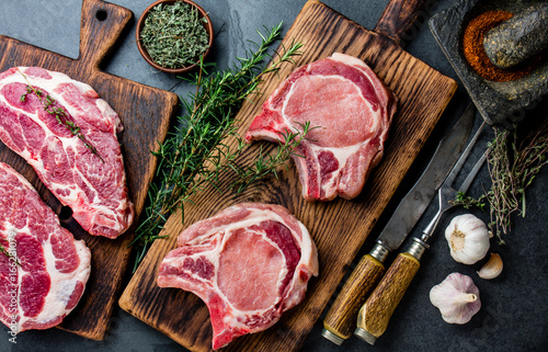 Raw pork cutlet chop for fry on grill and pan with herbs, garlic on wooden boards, slate gray background photo