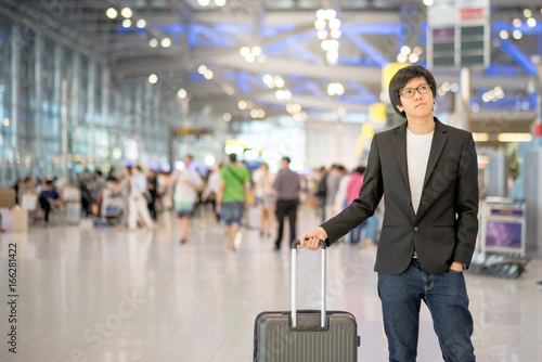 Young asian man with his suitcase luggage waiting for airline flight in the international airport terminal, business travel concept