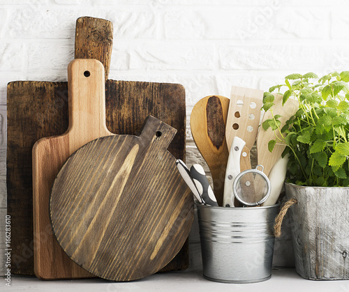 Kitchen still life on a white brick wall background: various cutting boards, tools, greens for cooking, fresh vegetables. Selective focus. photo