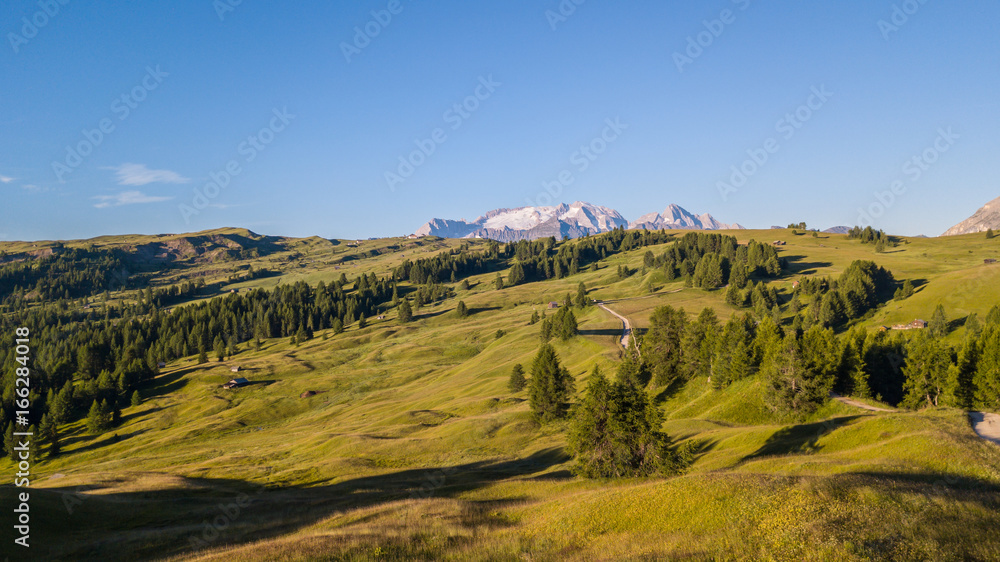 Fototapeta premium Aerial drone landscape of the meadows at high altitudes, forming gentle hills. Marmolada in the background. Dolomites, Alta Badia, Sud Tirol, Italy
