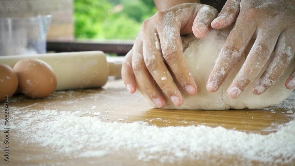Female hands kneading dough in flour with green tree blurred background Female hands kneading dough in flour with green tree blurred background