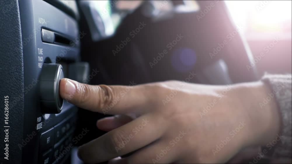 Close-up of female hand adjusting button audio on a vehicle's dashboard. Close-up of female hand adjusting button audio on a vehicle's dashboard.