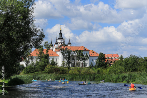 Group of people canoeing on the Narew river at the bottom of the hill with the monastic complex with defensive features from 16th and 17th century, Podlasie region, Suprasl, Poland