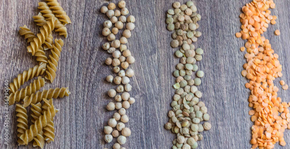 A wooden spoon surrounded by chickpeas, wholemeal pasta and a red and dark lens on a wooden background A wooden spoon surrounded by chickpeas, wholemeal pasta and a red and dark lens on a wooden background