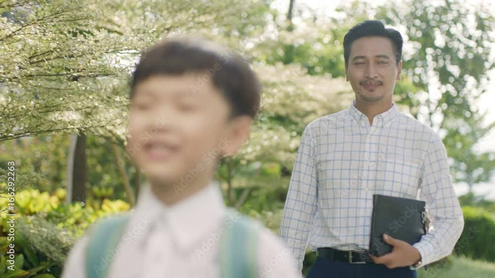 Asian boy walking through garden to school with father back lit in slow motion Asian boy walking through garden to school with father back lit in slow motion