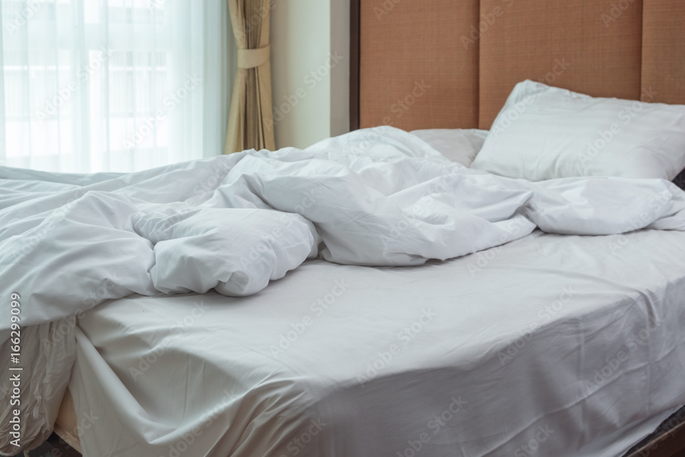 Morning sunlight falling on the bed with a crumpled bedding sheets and pillow through the window. Unmade bed with 3 white pillows and duvet after waking up on wooden background. Messy bed concept Morning sunlight falling on the bed with a crumpled bedding sheets and pillow through the window. Unmade bed with 3 white pillows and duvet after waking up on wooden background. Messy bed concept