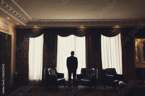 Lonely man stands before the window in a room