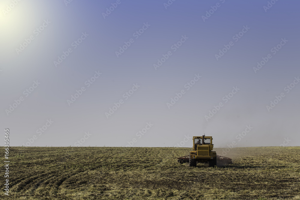 Fototapeta premium Tractor ploughing a field with a trail of dust behind it