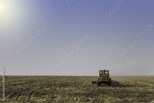 Tractor ploughing a field with a trail of dust behind it