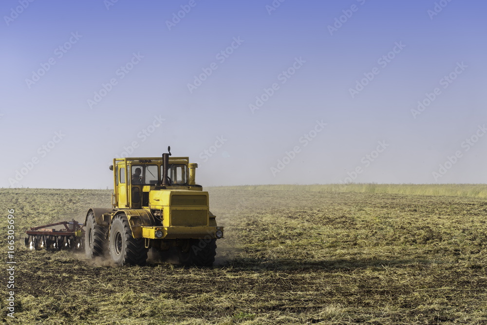 Tractor ploughing a field with a trail of dust behind it Tractor ploughing a field with a trail of dust behind it