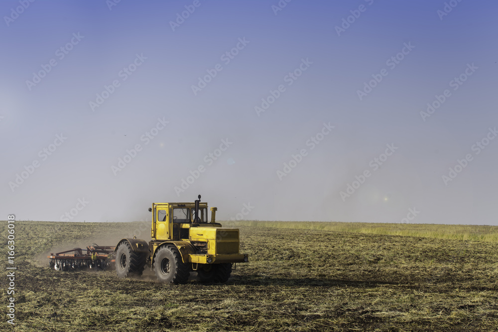 Fototapeta premium Tractor ploughing a field with a trail of dust behind it